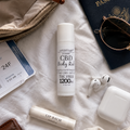 CBD body rub and lip balm on a white surface with sunglasses, passport, and earbuds.