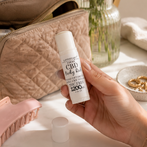 Hand holding a CBD body roll-on next to a cosmetic bag and beauty products on a marble surface.