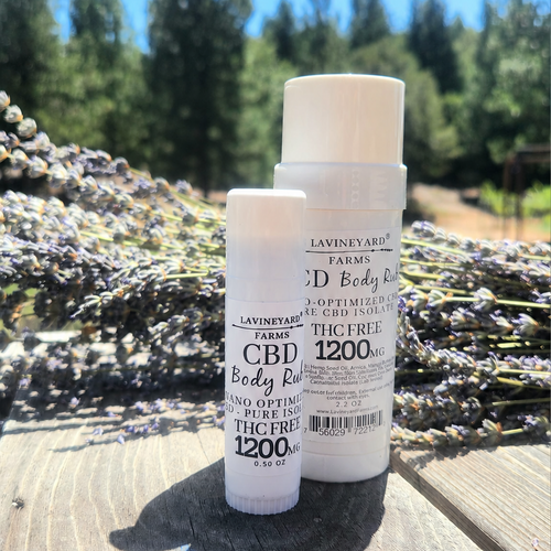 Two CBD body rub bottles from Lavineyard Farms on a wooden surface with lavender in the background.