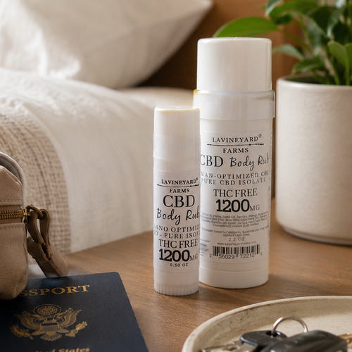 Two bottles of Lavineau CBD Body Lotion on a table with a passport, keys, and a plant in the background.
