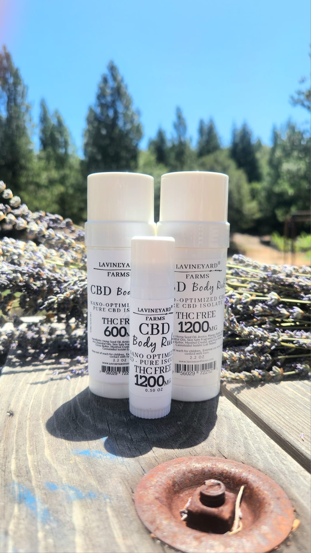 Three bottles of LAVINEYARD Farms CBD body lotion on a wooden surface with lavender in the background.